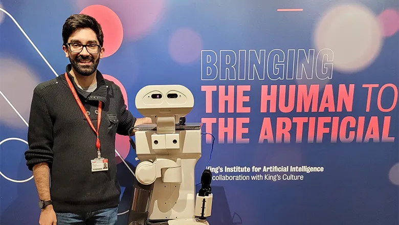 A man and a robot standing in front of a poster which reads 'Bringing the human to the artificial'
