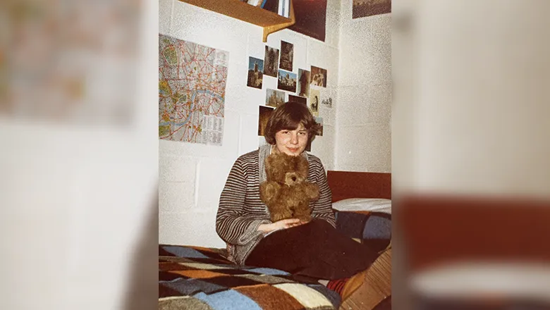 an Image of Ann in her student accomodation. She is sat on her bed, holding a small teddy.
