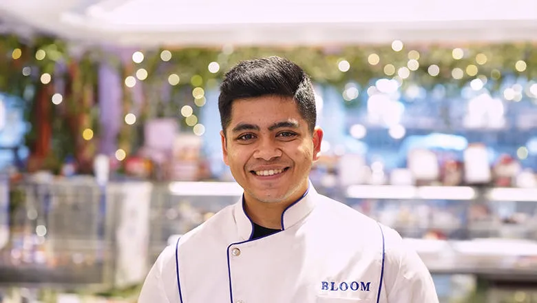 Parth Gupta smiles warmly in his chef whites. Behind him, lights twinkle.