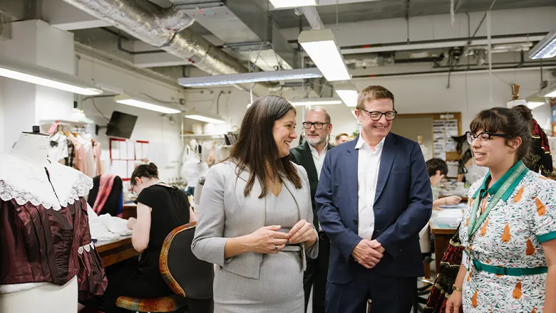 A man in a suit in a busy costume-making department with two smartly dressed women