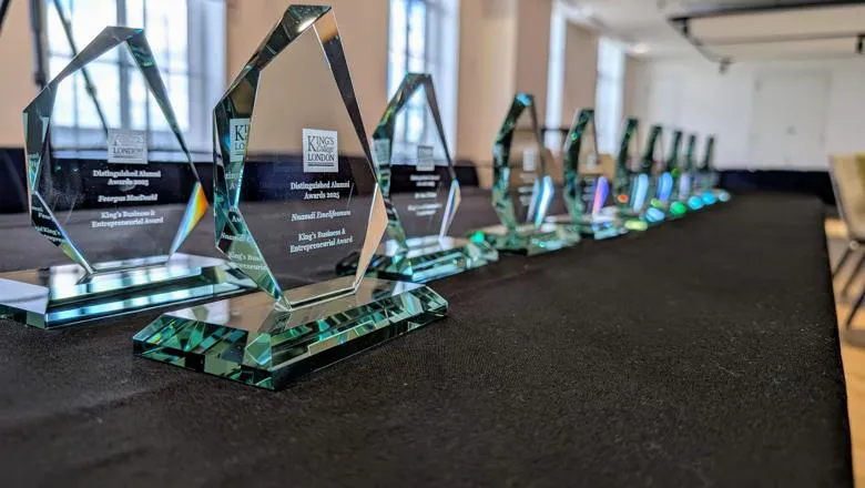 A row of awards sit on a table with a black cloth draped over it at an awards ceremony