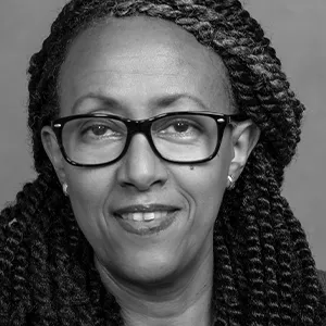 Dr Souci Frissa with braided hair wearing large black glasses, smiling slightly.