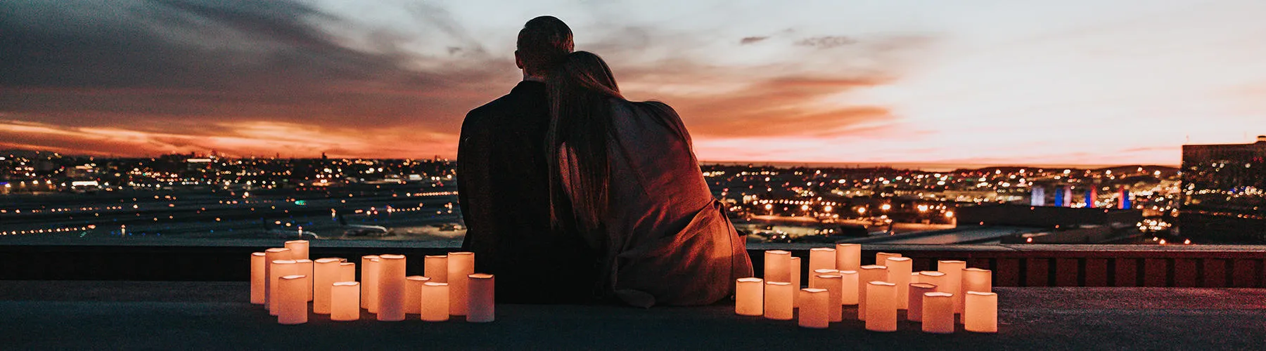 A couple sitting together with candles surrounding them overlooking a skyline