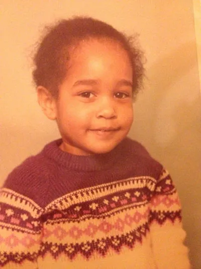 A photo of a young child smiling at the camera. She has dark hair and she is wearing a patterned jumper 