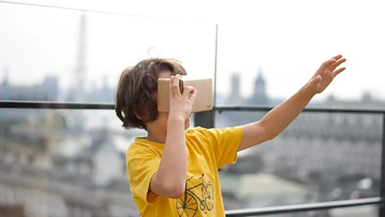 A child holds a virtual reality headset to his eyes and reaches out