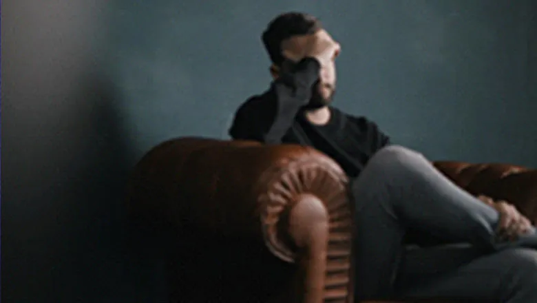 Stock image of man sitting on a sofa with a hand over his face