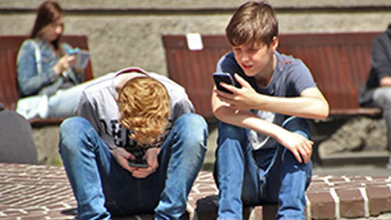 Two young boys sitting next to each other look at smartphones