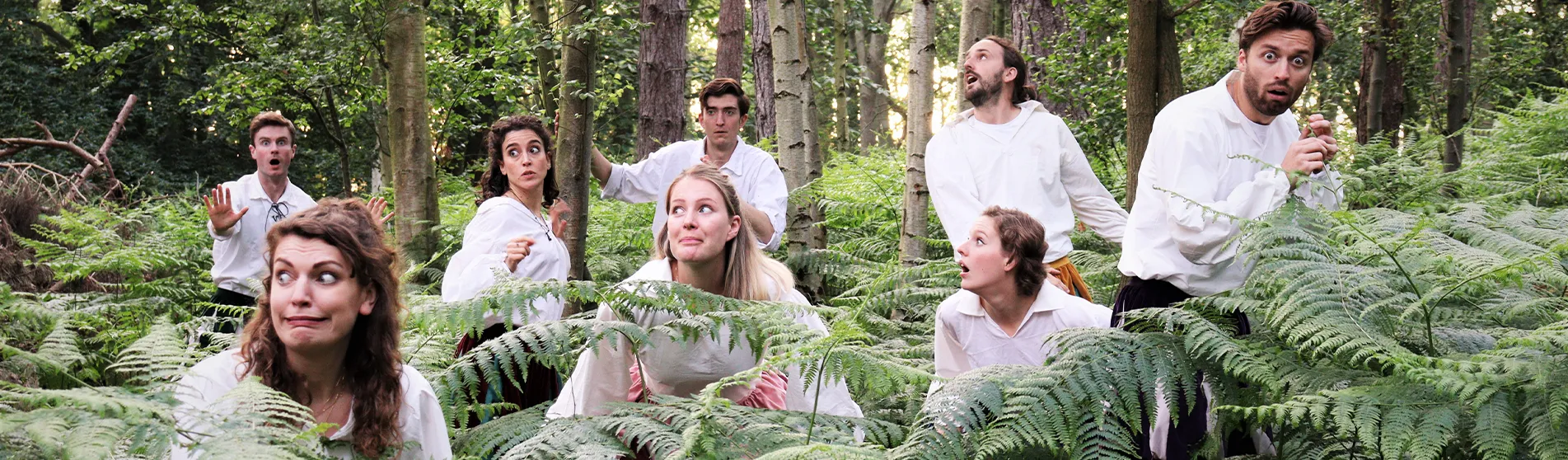 Dressed in Elizabethan costumes, the eight cast members of ShakeItUp Theatre pose in a forest setting