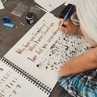 A woman write calligraphy onto a white booklet.