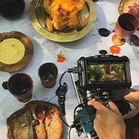 A camera is held over a table covered in cups and plates of food.