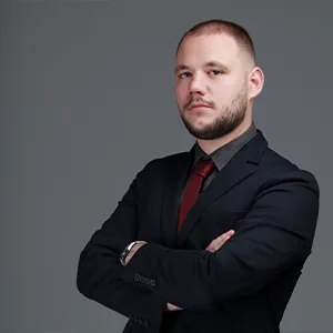 Kaloyan with arms folded, wearing a black suit jacket, red tie and grey shirt