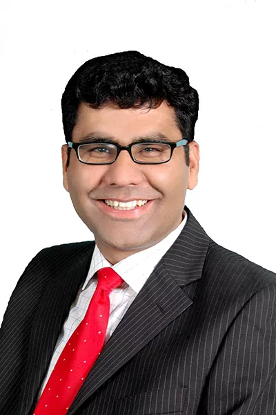 An image of Dr Quraish Khan, a graduate of King's College London with a master's degree in Criminology and Criminal Justice. He is wearing a black pinstripe suit, a white shirt, and a red tie.