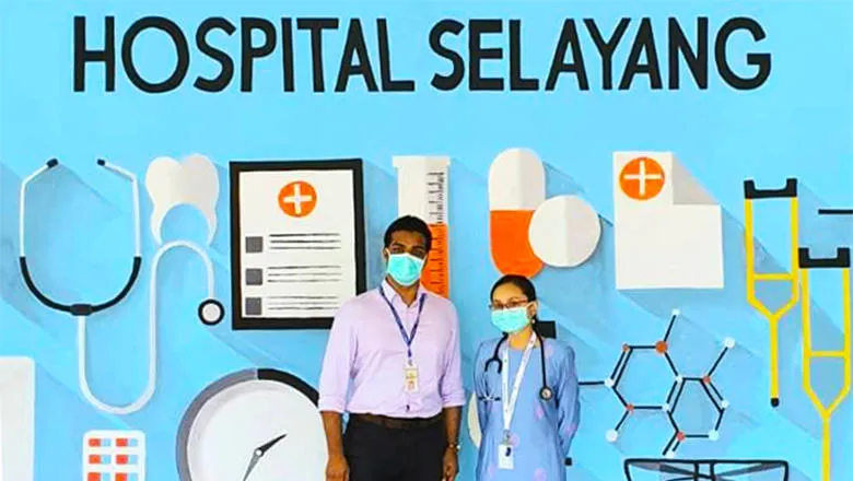 Two doctors with facemasks on stand in front of a blue background with 'Hospital Selayang' written above their heads