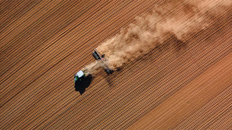 A tractor fixed with a plough kicks up a cloud of dust.