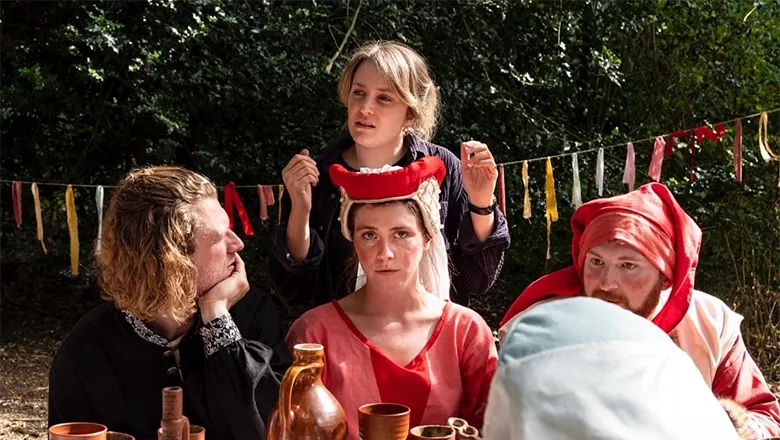 A group of three actors wearing medieval dress listen to their director, who stands in the background.