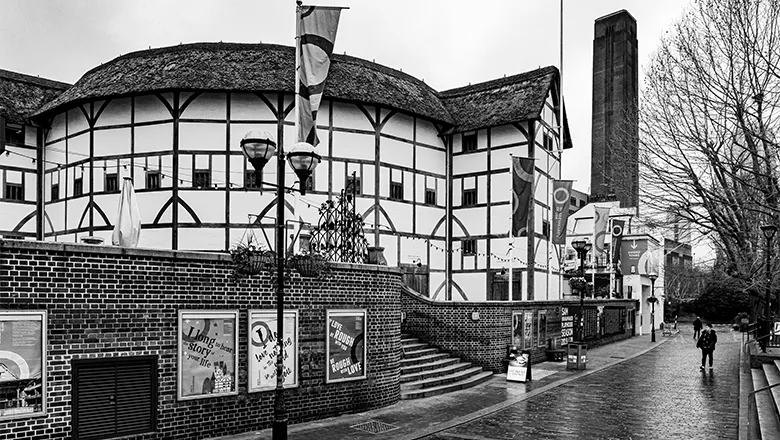 A black and white image of The Globe Theatre in London, an Elizabethan building with an iconic circular structure, taken from the outside.