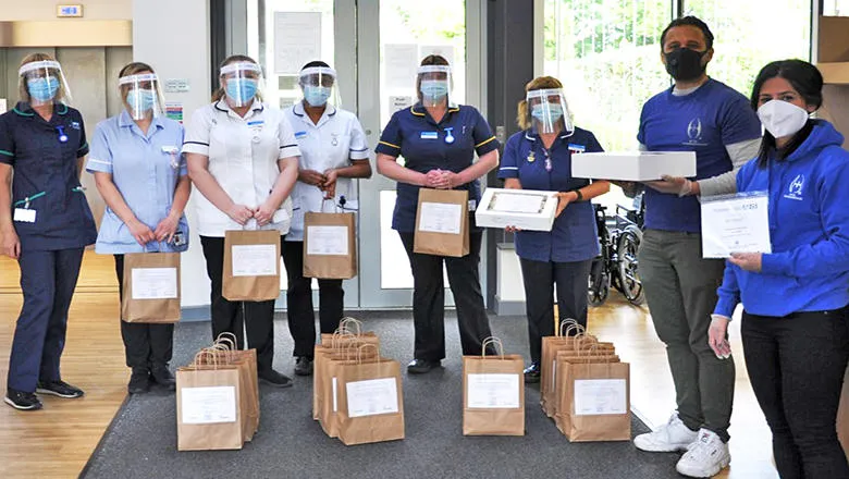 A group of health workers stand wearing PPE and holding paper bags.