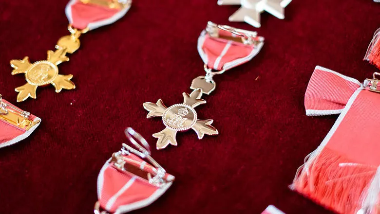 A silver medal, attached to a red ribbon with a white stripe, resting on a red cushion.
