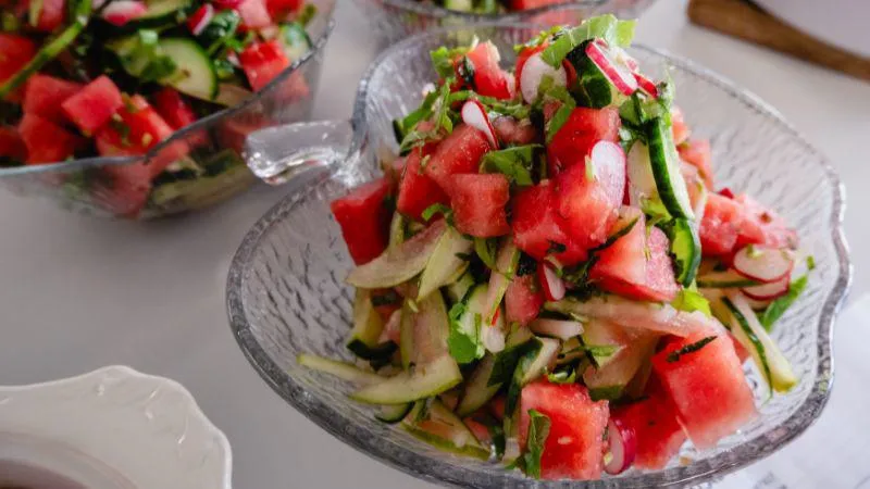 Fresh watermelon salad with cucumber, radish, onion, and herbs served in a clear glass bow