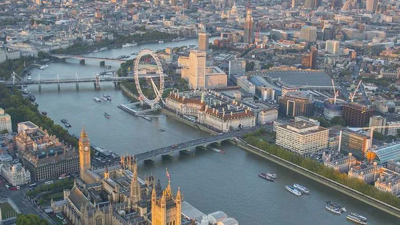 An aerial eastern view of London from above the River Thames with notable landmarks like Westminster, Big Ben and the London Eye present. 