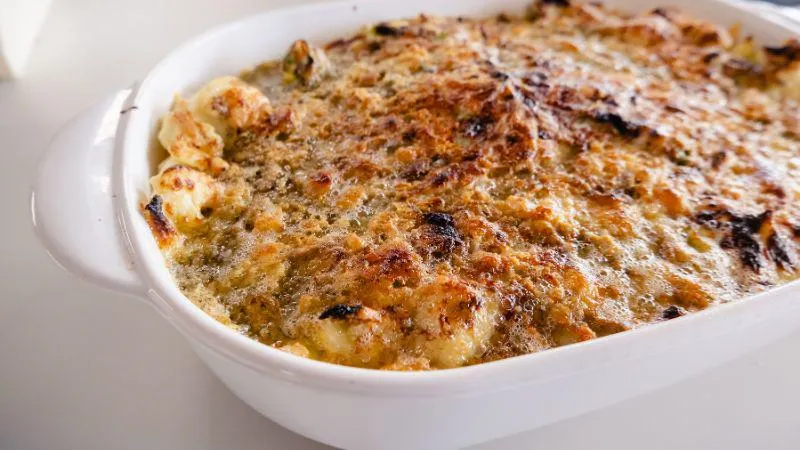 Golden-brown cauliflower cheese bake in a white ceramic dish, with a crispy top layer