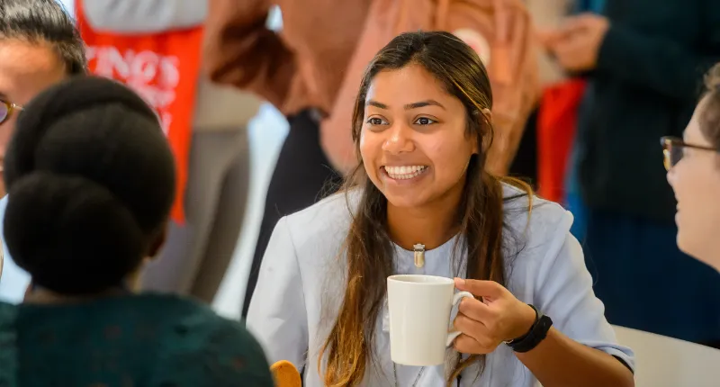 student holding tea chatting at event