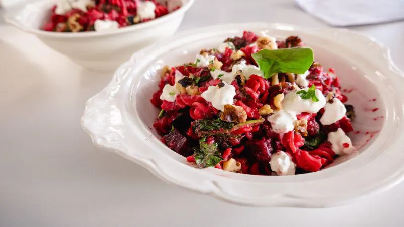 A white bowl filled with vibrant beetroot pasta, topped with cottage cheese.