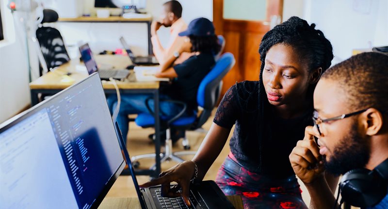 Two young people work together in front of one computer screen.