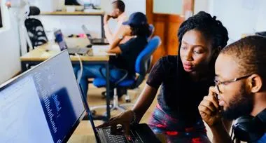 Two young people work together in front of one computer screen.