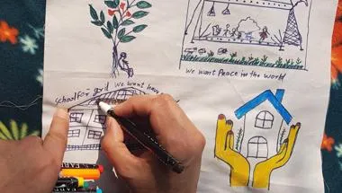 A child draws pictures about what they want in the future, including peace in the world and a school for girls