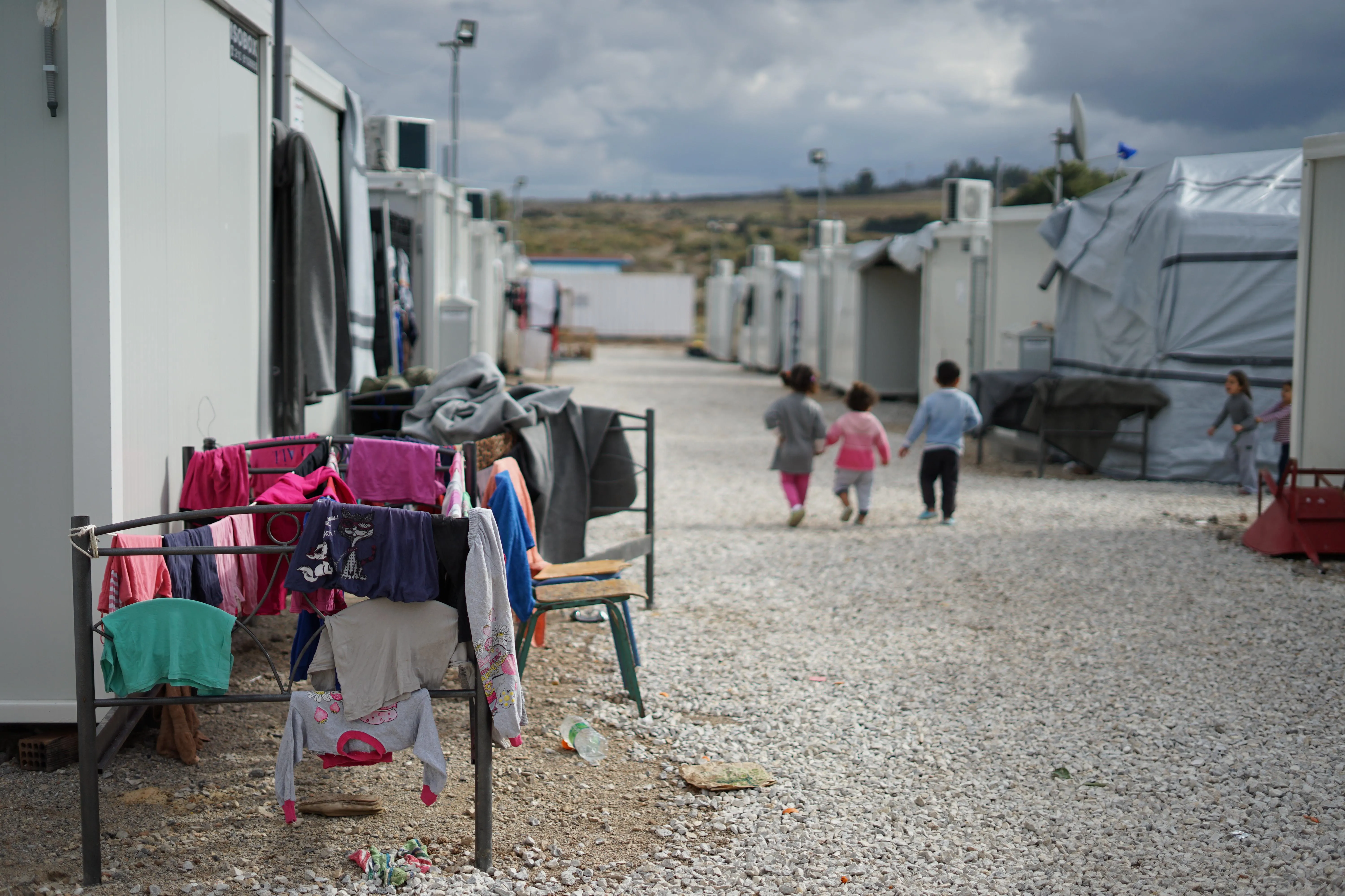 Three young children walk in a refugee camp.