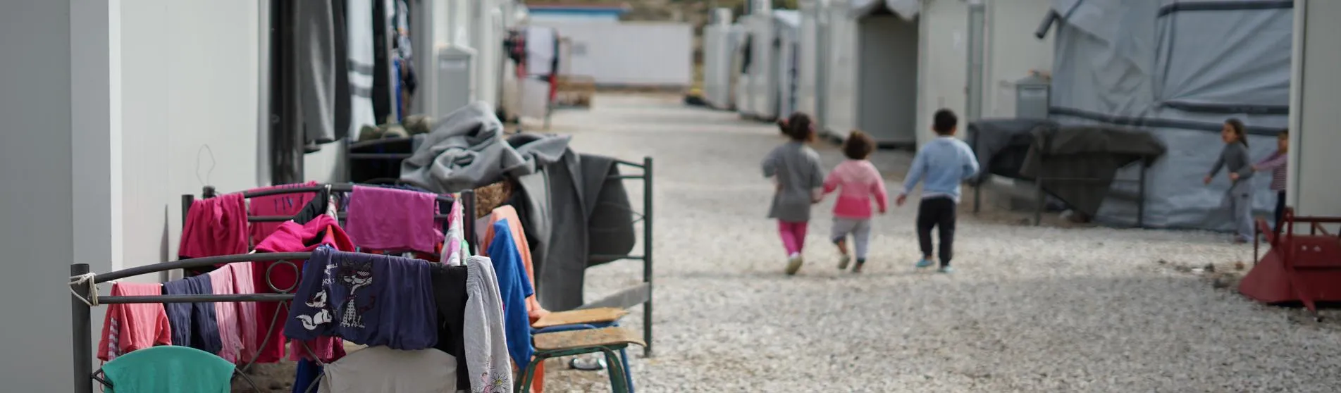 Three young children walk in a refugee camp.