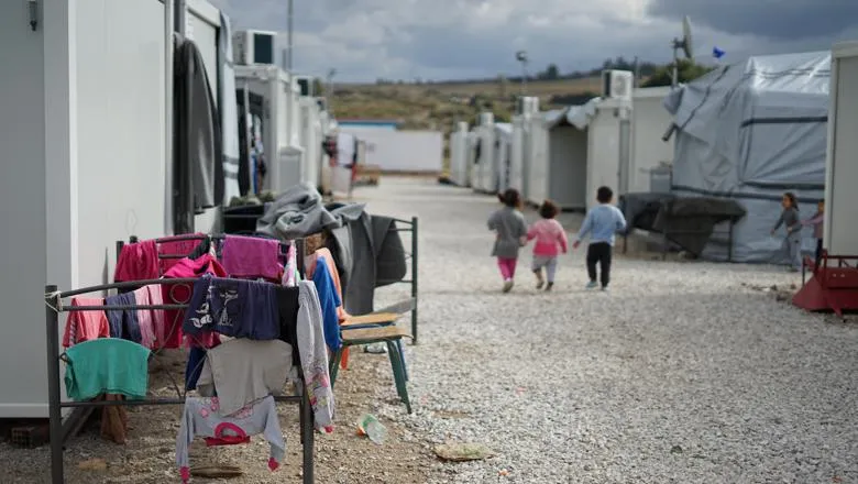 Three young children walk in a refugee camp.