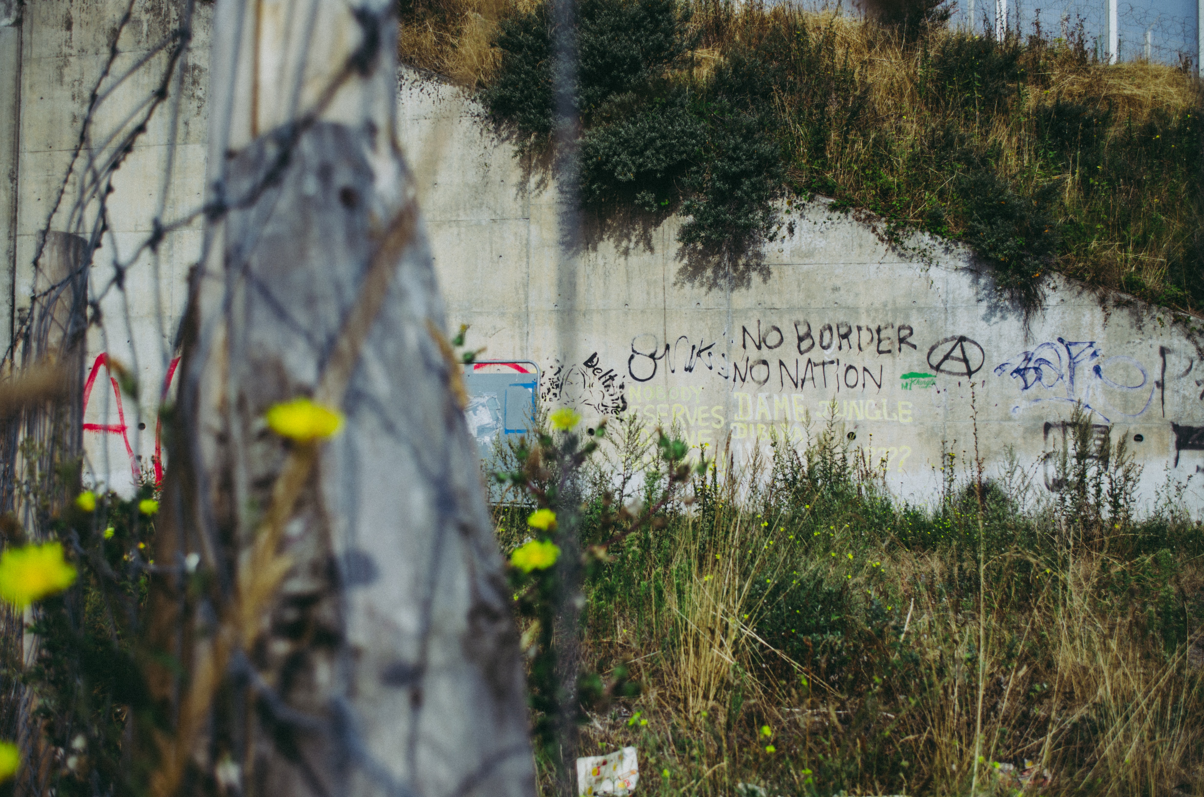 Graffiti on a dirty wall, near barbed wire and an abandoned tent