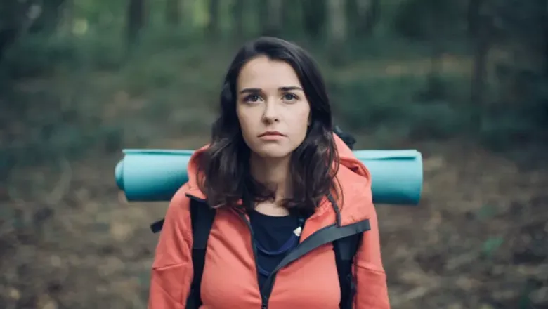 girl carrying camping equipment through forest