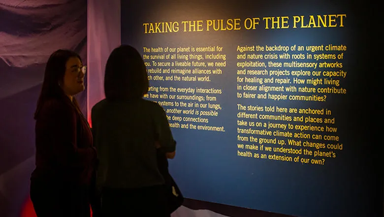 Two people looking at a exhibition sign with the title Taking the Pulse of the Planet Panel