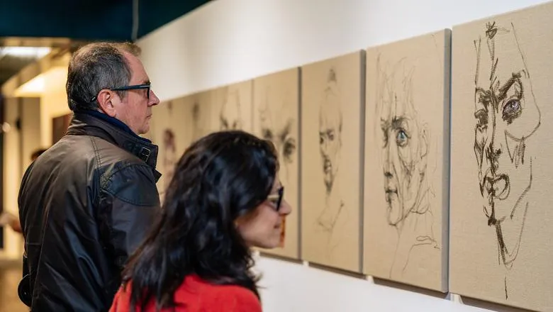 Two people looking at a series of portraits painted by Sara Shamma