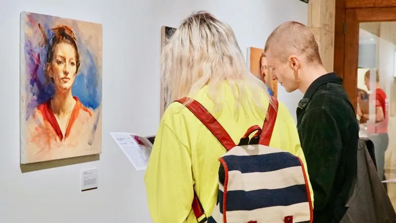 Two people looking at a portrait painting in the exhibition