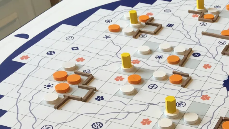 Image of a board game with squares, lines, orange puns, cards and dice