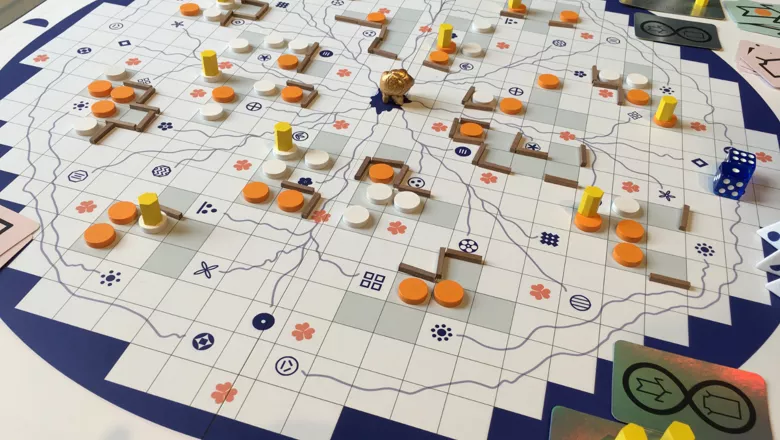 Image of a board game with squares, lines, orange puns, cards and dice