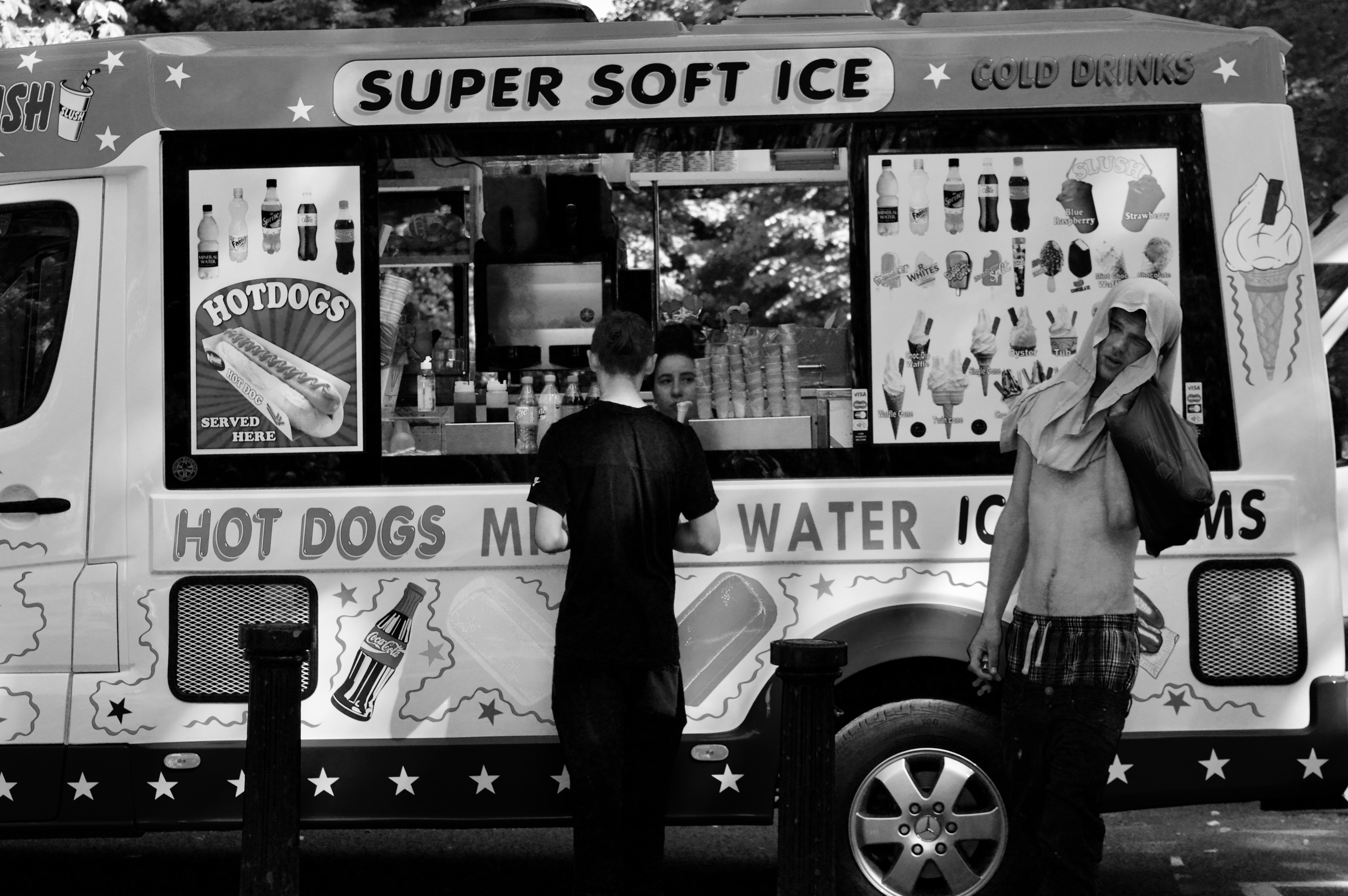 two boys buying ice creams from an ice cream van. one boy looks at the camera, squinting.