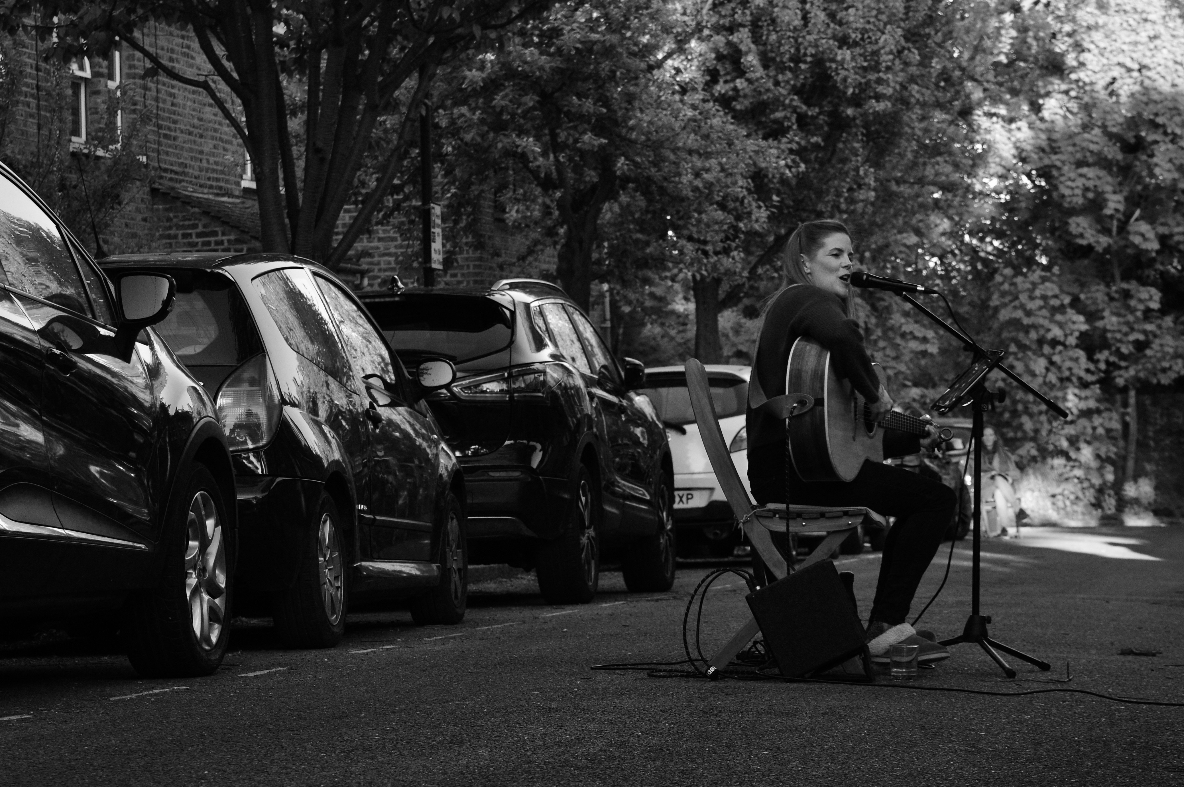 girl playing guitar in the middle of a residential street with parked cars behind her