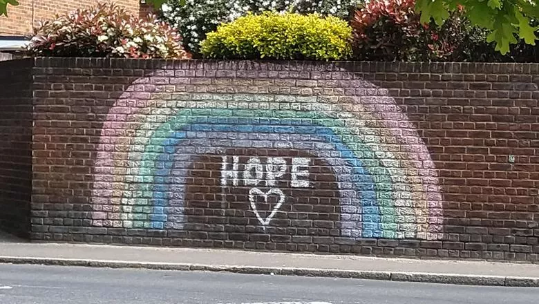 rainbow drawn in coloured chalk on a brick wall with the word 'hope' written in white chalk