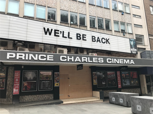 Photo of the front of the Prince Charles Cinema in Leicester Square. The front door is boarded up and the sign over the entrance says "We'll be back".