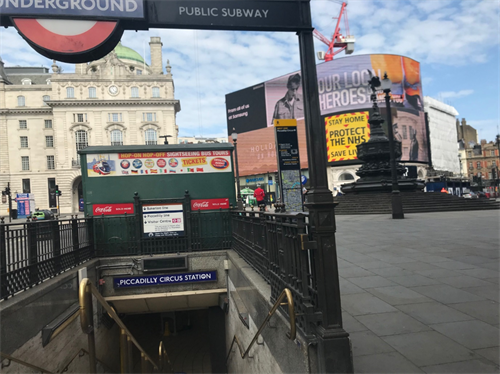 Photo of a pavement entrance to picadilly circus tube station with billboards behind.