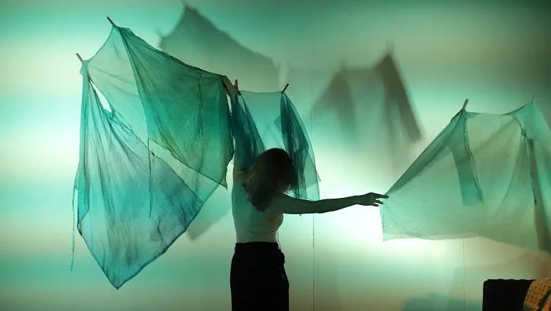 A female performer facing away from the camera and holding fabric in both hands that is hanging from the ceiling