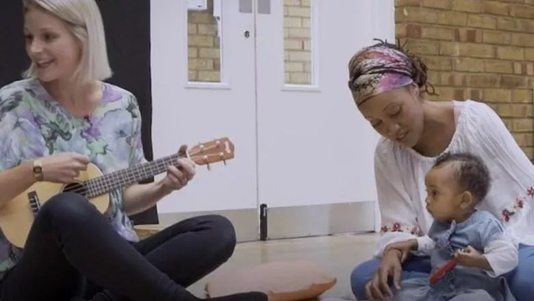 A person playing the ukulele and a mother and her baby listening.