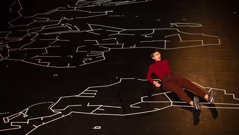 A person laying on a black floor with a map of the world drawn in white tape