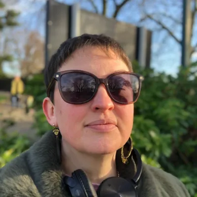Woman with short hair and sunglasses in front of building with sky background