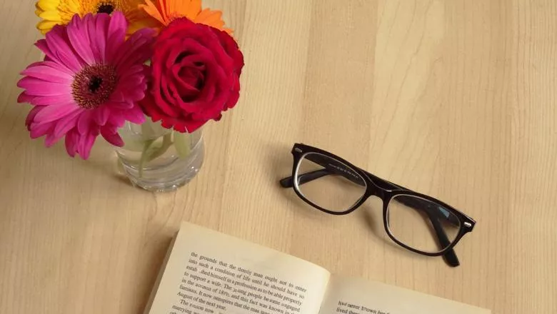 Flowers in a vase with glasses and open book on table
